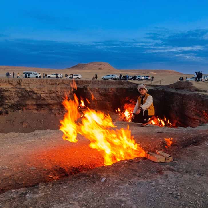 Happy tourists posing near the burning Darvaza gas crater at sunset in Turkmenistan